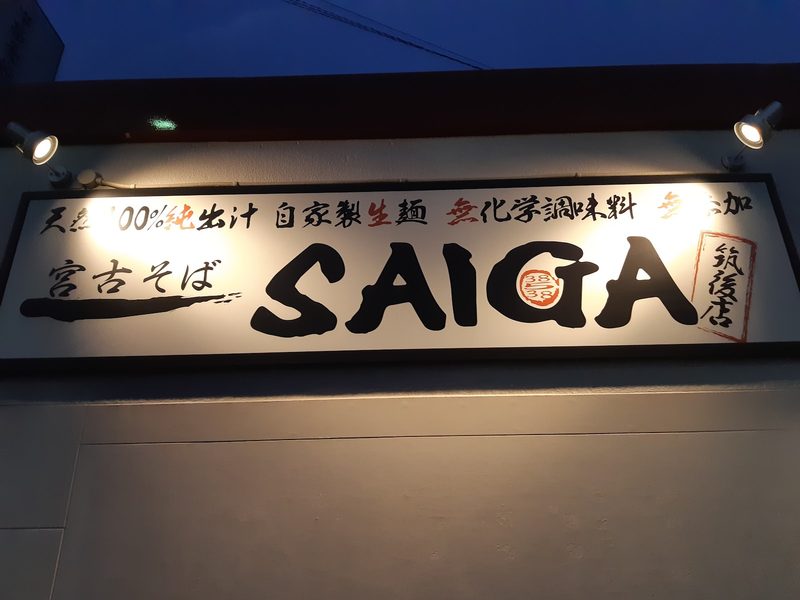 夕暮れにライトで照らされた「宮古そば SAIGA」の看板
