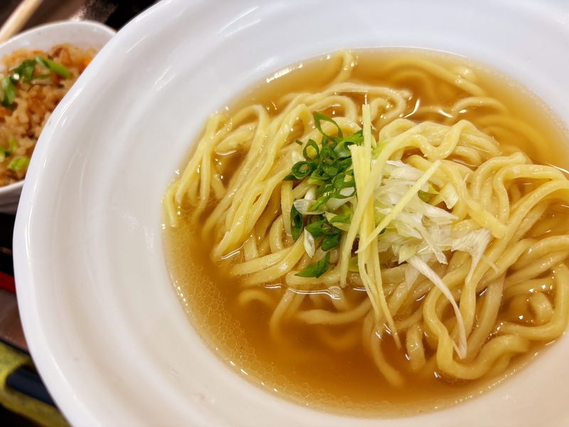 澄んだスープの中の太めの麺とネギのアップ
