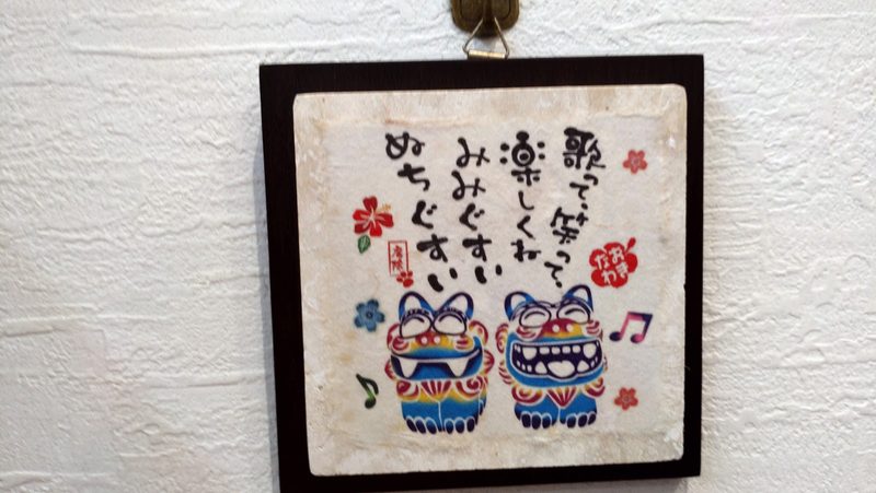 壁に飾った、シーサーの絵と文字の額